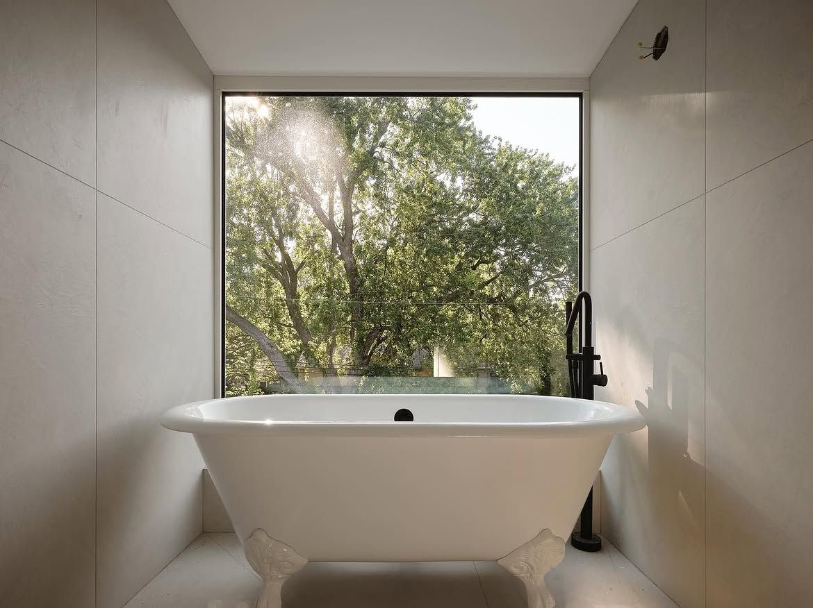 Salle de bain terminée : bain sur pattes devant une grande fenêtre donnant sur les arbres