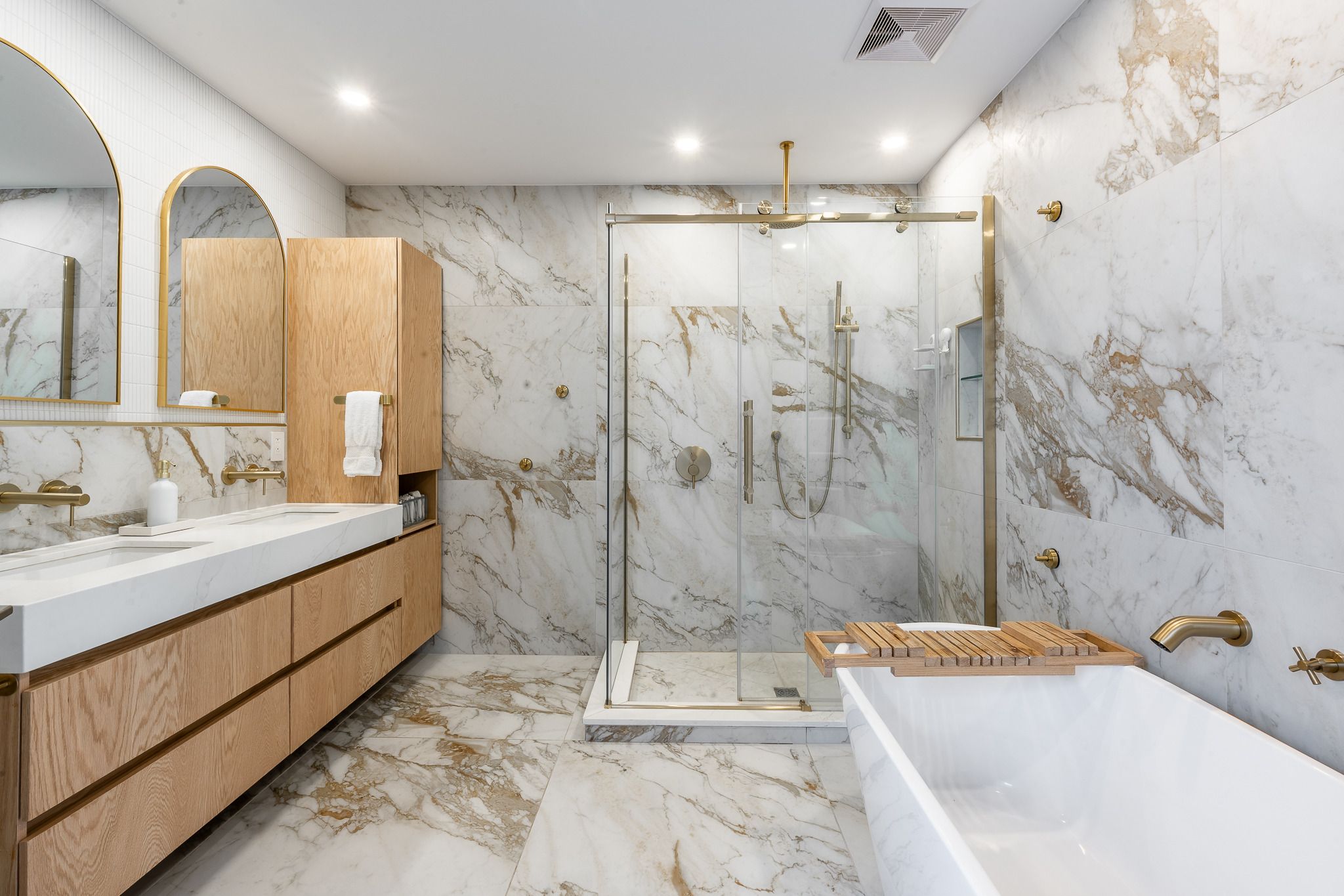 Salle de bain rénovée : murs en marbre, douche vitrée et vanité en bois clair