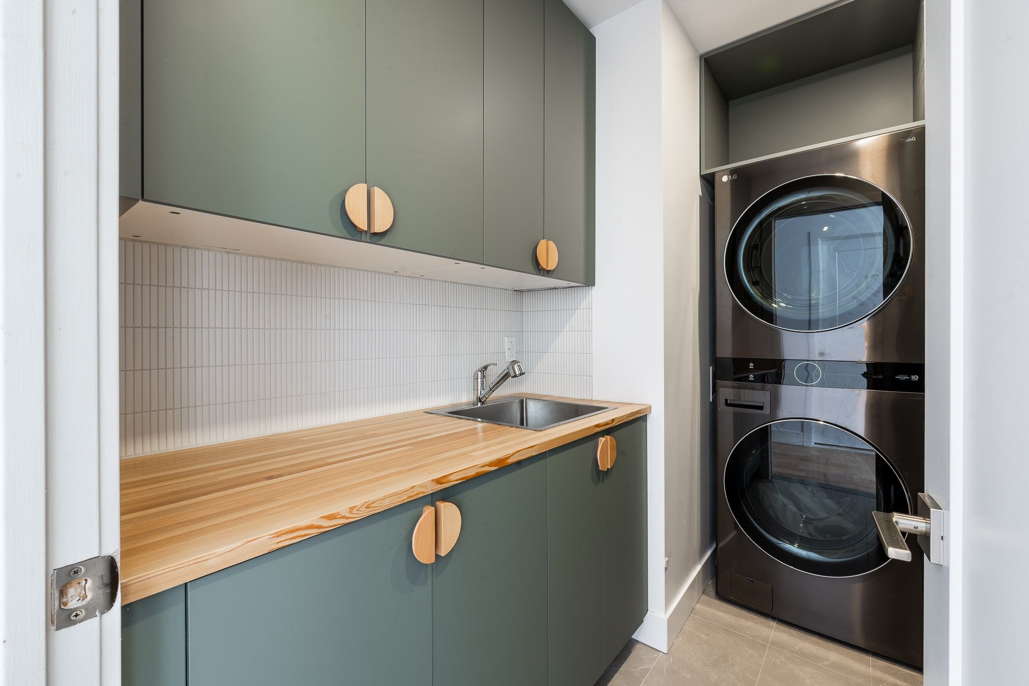 Salle de lavage rénovée à Rosemont : armoires vertes, comptoir en bois et laveuse-sécheuse superposées