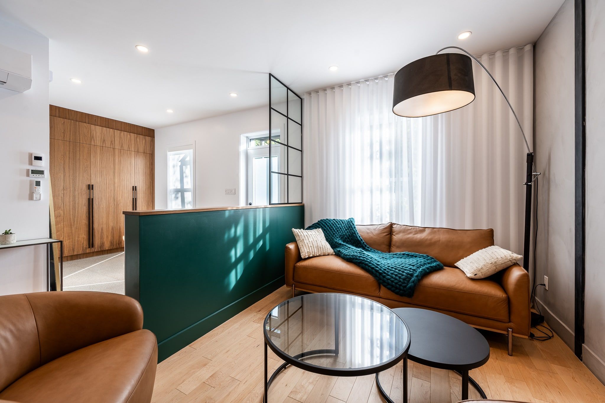 Salon rénové à Rosemont : canapé en cuir devant un demi-mur vert et une verrière noire
